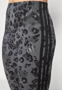 Leggings atletici grigi con motivo a leopardo nero. Presentano tre strisce nere lungo il lato e un logo metallizzato sull'anca.