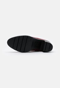 Roter Lederschuh mit einer strukturierten schwarzen Gummisohle, die Rillen und Muster für besseren Halt bietet. Elegantes Design mit einer abgerundeten Zehenform.