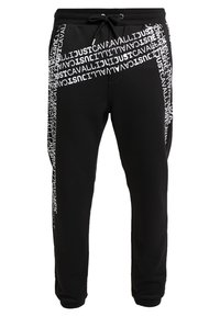 Black sweatpants with white "JUST" text pattern, adjustable drawstring waist, and ribbed cuffs. Smooth texture and athletic fit.
