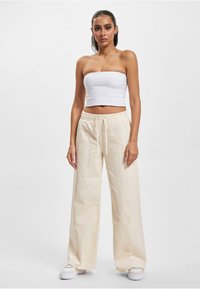 Beige weite Cordhose aus Cord mit einem elastischen Bund, kombiniert mit einem weißen, taillierten trägerlosen Oberteil und weißen Plateauschuhen.