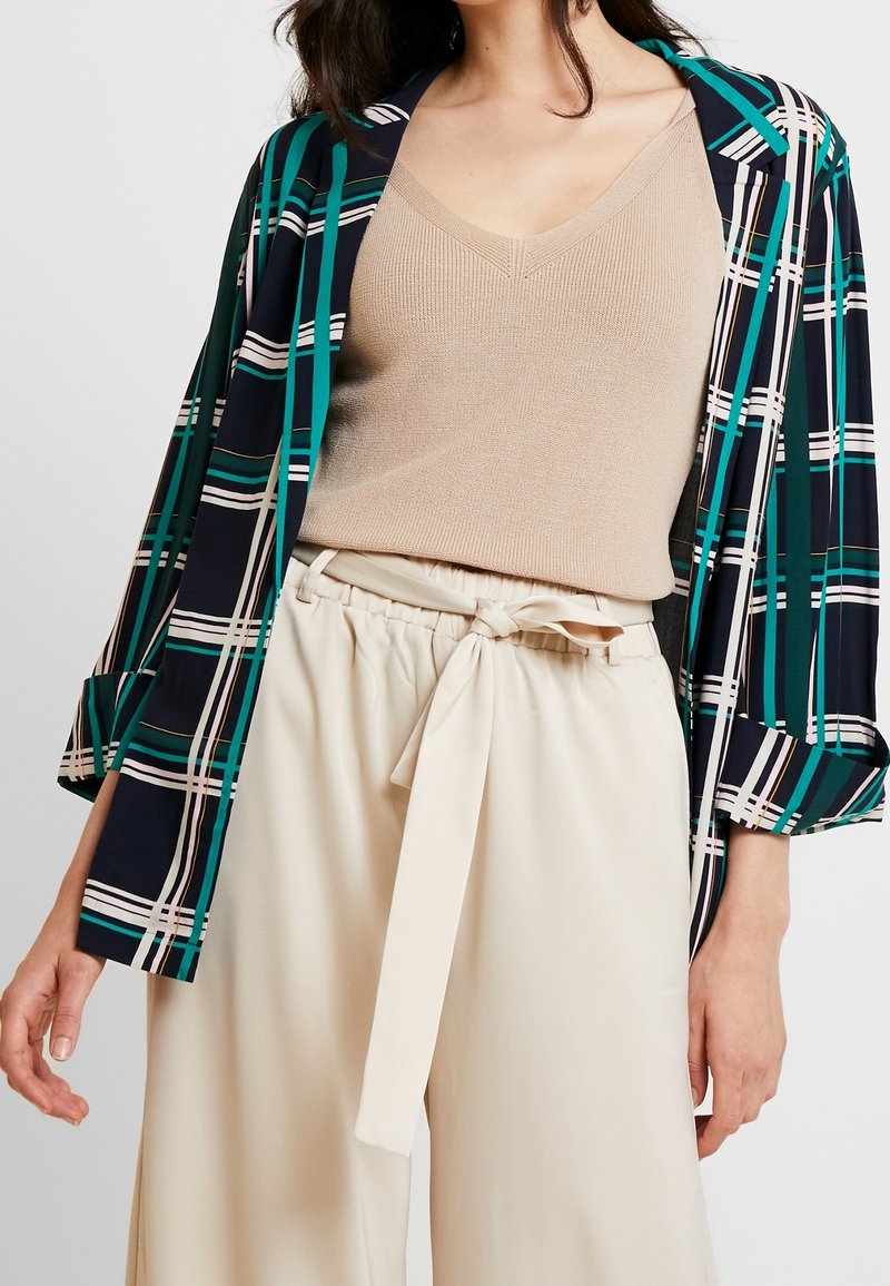 Lehký kimono vzorovaný v námořnické modré a zelené, s širšími rukávy, přes obtažený béžový žebrovaný top a krémové kalhoty s vysokým pasem a opaskem.