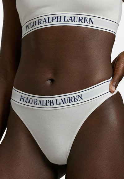 Weißer Baumwoll-String mit einer gerippten Struktur und einem breiten Bund, der oben den Schriftzug "POLO RALPH LAUREN" in Dunkelblau trägt.