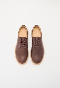Brown leather oxford shoes with rounded toe, minimal stitching, and flat laces. Inside features a beige lining with embossed brand name.