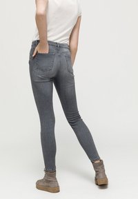 Jeans gris de corte slim con dos bolsillos traseros, textura de mezclilla suave y diseño de cintura alta, combinados con botas tobilleras gris claro.