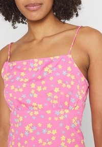 Pink floral dress featuring small yellow and blue flowers, thin straps, and a fitted bodice with a slightly gathered waist.