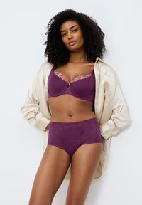 Fialová podprsenka s krajkovým lemem a výřezem, doplněná květinovými kalhotkami s vysokým pasem, v kombinaci s béžovou saténovou košilí.
