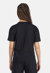 Camiseta de algodón negra con mangas cortas y cuello redondo; textura suave; sin patrones ni acentos visibles; corte estándar, combinada con pantalones negros.