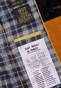 Etiqueta interior negra y dorada con texto, patrón cuadro gris, borde amarillo y etiqueta de cuidado blanca que representa utensilios de mesa e instrucciones.