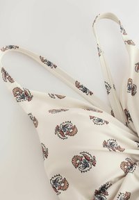 Maillot de bain blanc à motifs floraux avec des bretelles fines, présentant des designs complexes en bleu, rose et marron sur une surface en tissu lisse.