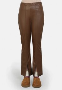Bruine faux leren broek met vooropeningen, voorzien van een gladde textuur en een recht gesneden ontwerp, gedragen met bruine slippers en patroonsokken.