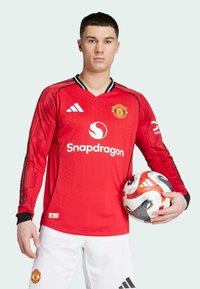 Rotes Longsleeve-Fußballtrikot mit V-Ausschnitt, schwarzen Akzenten und gemusterten Ärmeln. Das Logo und der Markenname sind auffällig platziert.