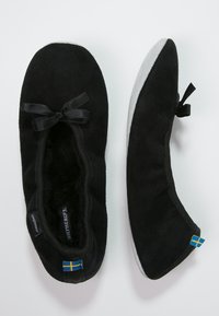 Black suede ballet flats with a soft gray sole, featuring a small bow accent and flag detail on the sides. Interior lined with soft material.