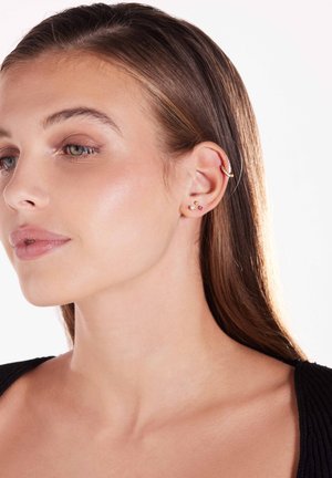 Boucles d'oreilles en argent présentées sur le haut de l'oreille, accompagnées de petites boucles d'oreilles en clous ornées de gemmes colorées dans un design minimaliste.