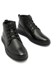 Czarne skórzane botki za kostkę z okrągłymi noskami, teksturowaną cholewką, przeszyciami oraz płaską gumową podeszwą. Zawierają sznurowadła i wsparcie kostki.
