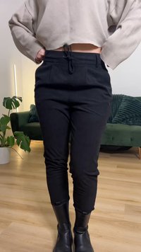 Black tapered pants with a drawstring waist, featuring front pockets. Worn with black knee-high boots. Cropped beige top above the waist.