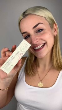 Veganskt kollagenögonserum i en ljusgrön rektangulär förpackning med botanisk design, hålls av en person som ler, klädd i en vit topp och guldsmycke.