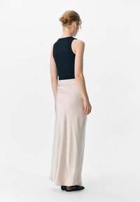 Zwarte mouwloze top en een vloerlange zachtbeige rok. De rok heeft een gladde textuur, met een subtiele val en zijnaden.