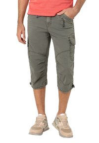 Cargo-Shorts aus olivgrünem Stoff, knielang mit mehreren Taschen, verstärkten Nähten und verstellbaren Säumen. Kombiniert mit beigefarbenen Sportschuhen.