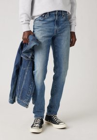 Blugi din denim de culoare albastră deschisă, cu o croială slim, design clasic cu cinci buzunare și ușoară decolorare. Asortați cu o jachetă din denim închis la culoare și adidași negri.
