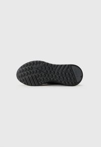 Suela de zapatilla negra con patrones de tracción circulares y rayados, con el logotipo "ARKK" cerca del talón sobre un fondo blanco.