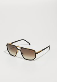 Solfanger med en svart og gull metallramme, geometrisk design, gradient brune linser og teksturerte svarte tempeltipper.