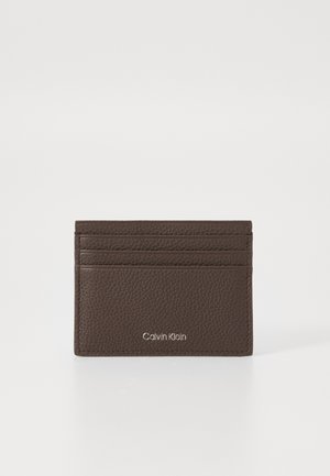 Brown pebbled leather cardholder with three card slots and Calvin Klein logo embossed in silver on front center.