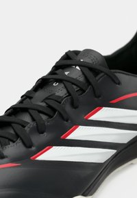 Μαύρο αθλητικό παπούτσι με μαύρα κορδόνια, τρεις λευκές ρίγες με κόκκινο περίγραμμα και υφασμένο μαύρο πέλμα.