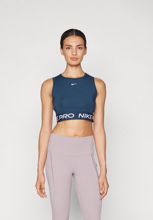 Un sutien sport cropped de culoare albastru marin cu un logo alb și o bandă cu text; asociat cu colanți lungi de culoare lila deschis cu talie înaltă și cusături laterale.