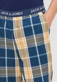 Medvilniniai languoti pižamos kelnės su mėlynomis, geltonomis ir pilkomis kvadratėliais. Turi elastinį juosmenį su prekės ženklu "JACK & JONES."