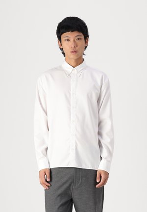 White long-sleeve button-up shirt with a collar, featuring a smooth texture and a classic fit; worn with dark gray trousers.
