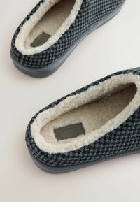 Knitted gray slippers feature a textured upper and soft cream lining. The sole is flat and gray, with a subtle brand tag inside.