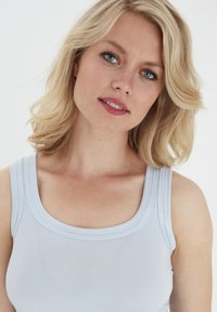 Világoskék ujjatlan felső sima anyagból, kerek nyakkivágással és széles pántokkal. A dizájn egyszerű, minta és díszítés nélkül.