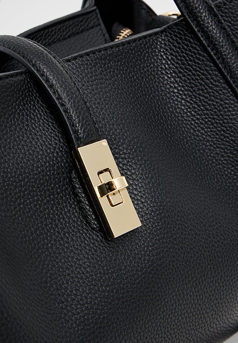 Schwarze, strukturierte Handtasche aus Leder mit einem goldenen, rechteckigen Verschluss. Verfügt über glatte Griffe und ein mit einem Reißverschluss gesichertes Innenfach für sicheren Stauraum.