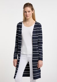 Cardigan blu navy con righe orizzontali bianche, apertura frontale, maniche lunghe e design a lunghezza intermedia, indossato sopra una maglietta bianca semplice.