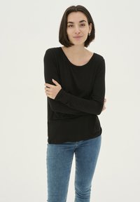 Fekete, hosszú ujjú felső kerek nyakkivágással, sima textúrával és laza szabással, kék skinny farmernadrággal párosítva. Egyszerű és sokoldalú dizájn.