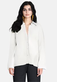 Camicia bianca con colletto, maniche lunghe e taglio dritto. Tessuto morbido con vestibilità leggermente ampia. Design minimalista.