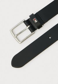 Svart lærbelte med en sølvfarget metallspenne, med Tommy Hilfiger-logo og pent søm. Jevn tekstur og avsmalnende ende-design.