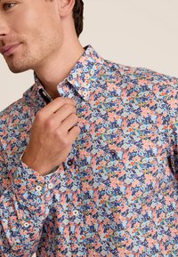 Bloemige blouse met knopen en een meerkleurig patroon, voornamelijk in blauw, roze en groen. Gemaakt van lichte stof met een standaardkraag.