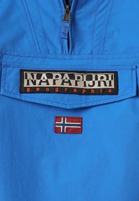 Veste bleue avec une fermeture éclair à l'avant, un patch logo Napapijri Geographic, et un petit patch drapeau norvégien sous la poche.