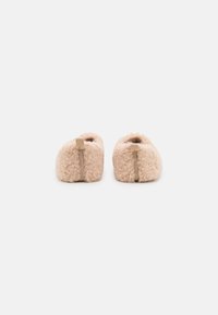 Soft, pale pink fuzzy slippers with a rounded shape, featuring a central seam and a small fabric tab at the back. Textured wool exterior.