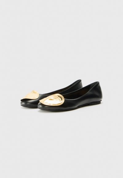 Svart skinnballerina med en tåhuvud i guldmetall och en slät yta. Har en minimalistisk design och låg profil.