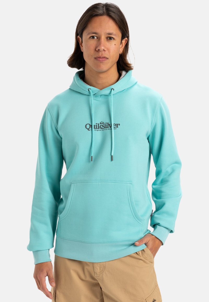 Sudadera color turquesa con un bolsillo tipo canguro, capucha ajustable con cordón y logo de Quiksilver en marrón oscuro en el centro. Textura suave.