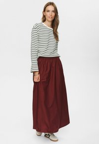Haut à manches longues rayé en blanc et noir, associé à une jupe maxi bordeaux avec une taille élastique, complété par des baskets blanches.