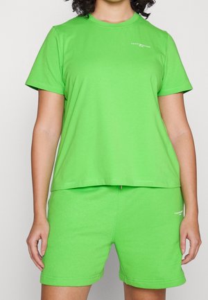 Persoon draagt felgroen T-shirt met korte mouwen en bijpassende shorts met kleine witte Tommy Hilfiger-logo's op borst en been.