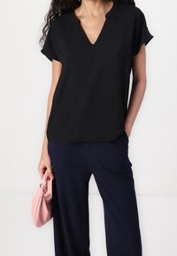 Haut noir à manches courtes avec un col en V et une coupe décontractée, fabriqué dans un matériau léger. Assorti à un pantalon bleu marine et un sac à main rose.