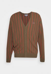 B brun cardigan med vertikala röda ränder, V-hals, knappstängning och liten Lacoste-logotyp på vänster bröst. Mjuk textur och figurnära design.