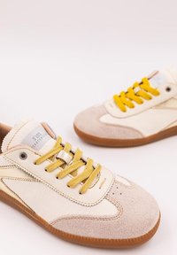 Sneaker crema e beige con un mix di camoscio e pelle, lacci gialli e suole in gomma. Presentano cuciture sottili e marchio sulla linguetta.