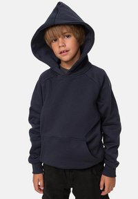 Felpa blu navy in tessuto morbido con una grande tasca frontale, polsini larghi e un cappuccio spazioso, indossata con pantaloni scuri.