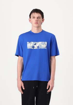 Blå bomulds T-shirt med et rektangulært hvidt patch med blå og sorte abstrakte mønstre. Korte ærmer og afslappet pasform.