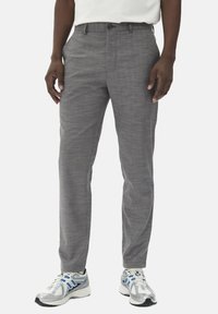 Pantalons gris fuselés en tissu texturé, avec une fermeture à un bouton et des poches latérales, portés avec des baskets de sport.